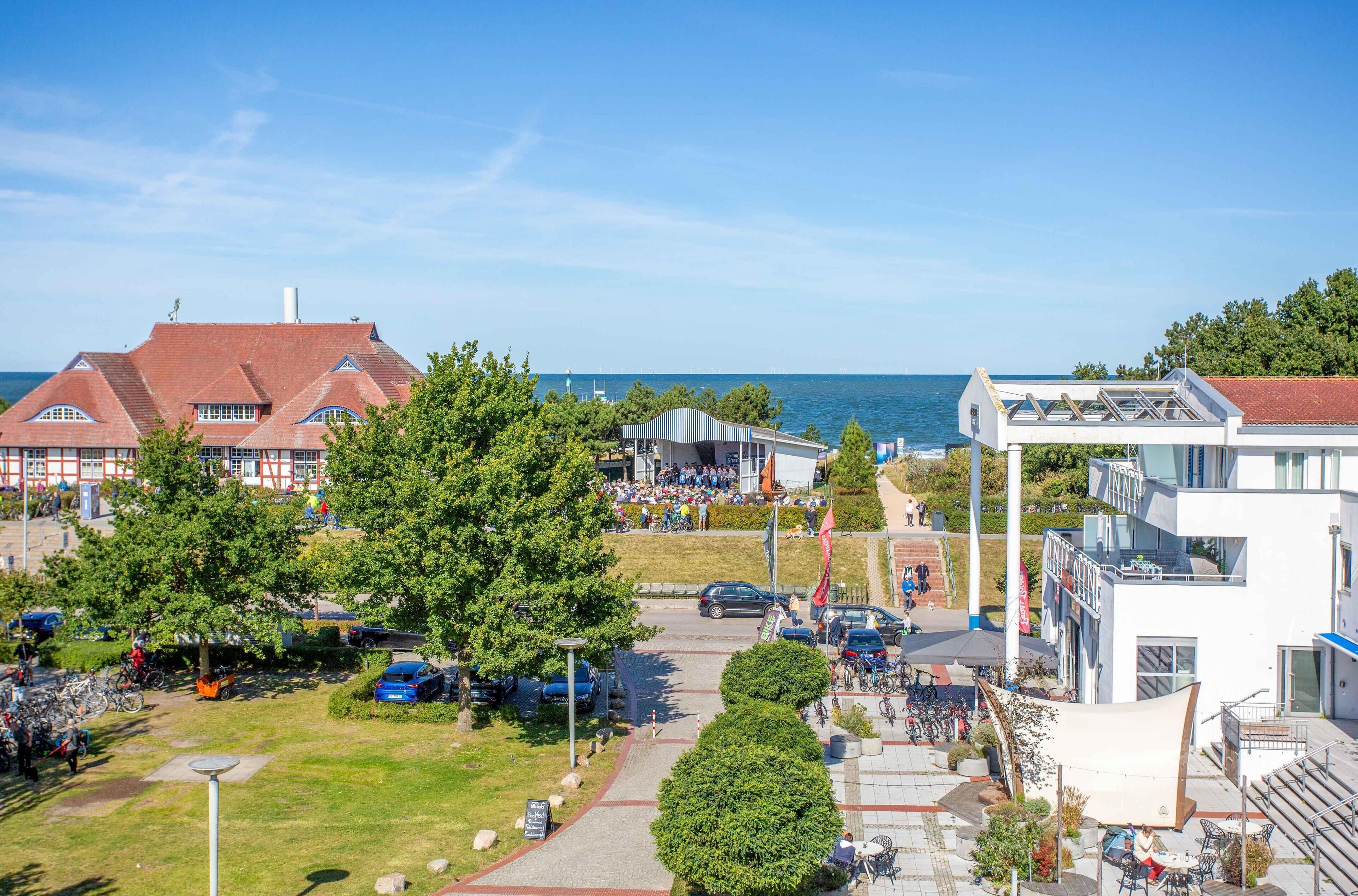 A coastal town with a mix of traditional and modern buildings, a central square with seating, and a view of the sea.