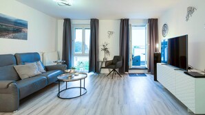 A modern living room with a sofa, coffee table, TV, and a view through the window. - 5-Star "Ostseeperle" Vacation Apartment in Zingst, Next to the Pier (Zingst)