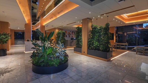 A modern lobby with a central planter, glass walls, and a seating area.