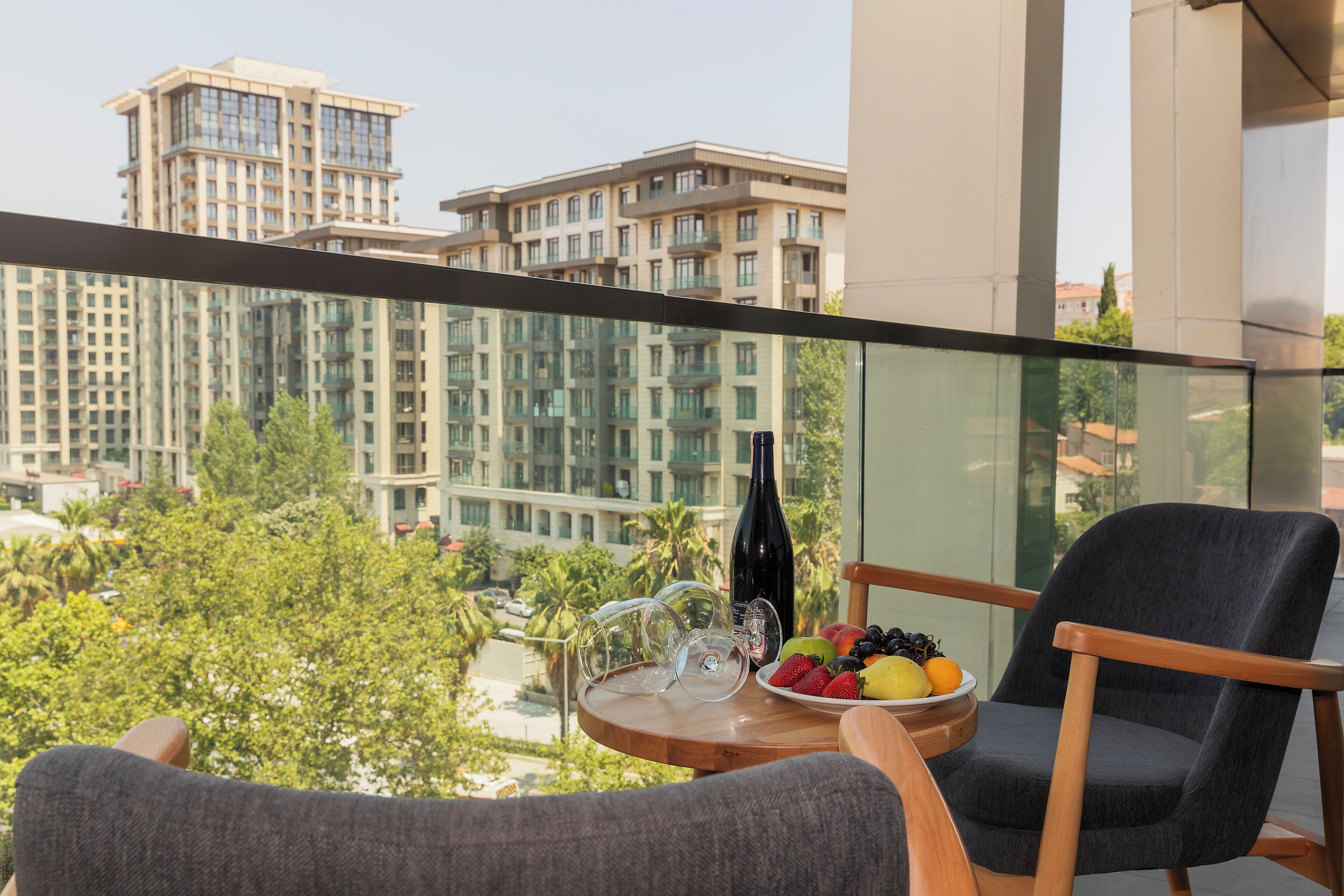 Un balcón con vistas a edificios altos, una mesa con una botella, vasos y fruta.