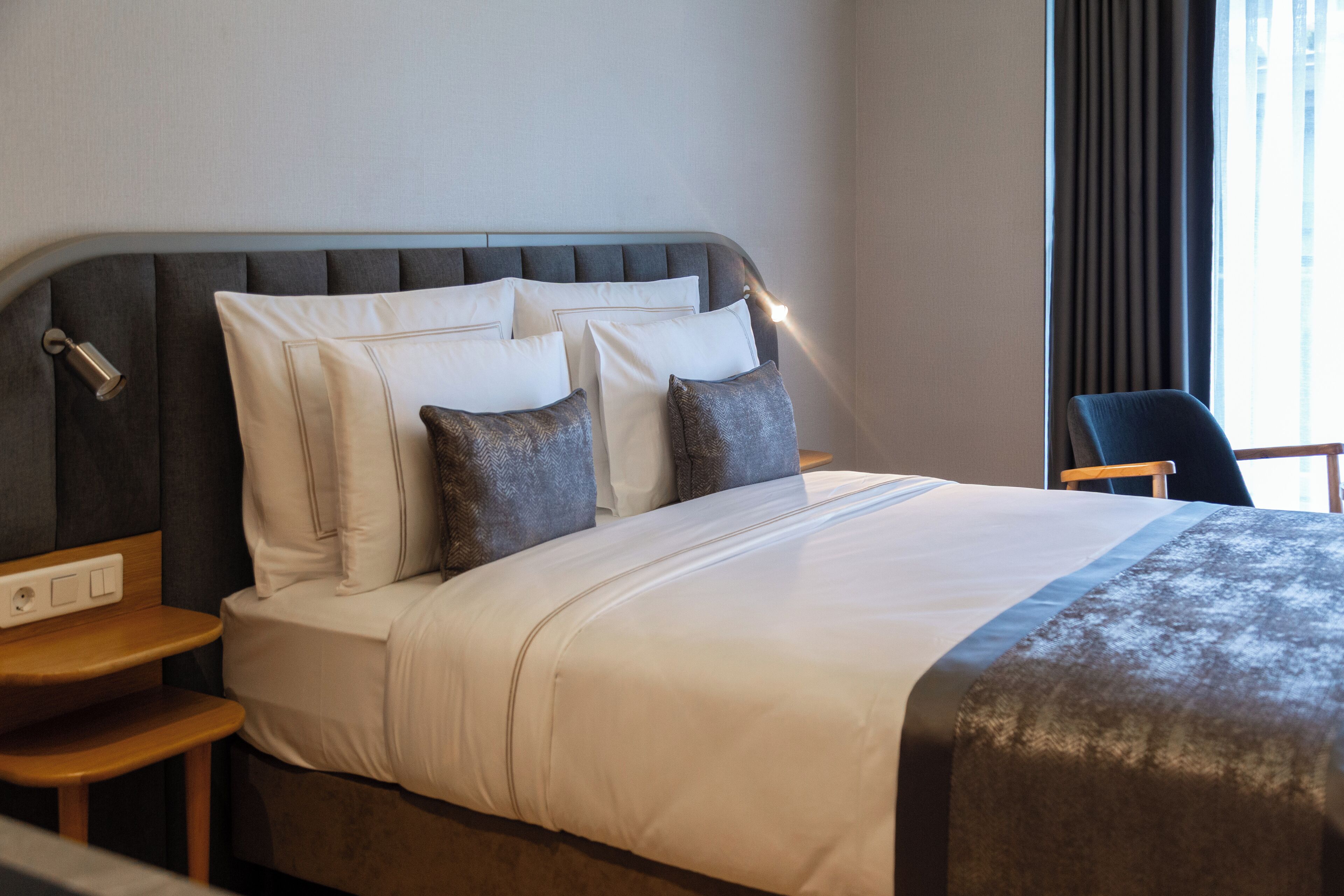 A neatly made bed with white and gray bedding, a wooden nightstand, and a chair.