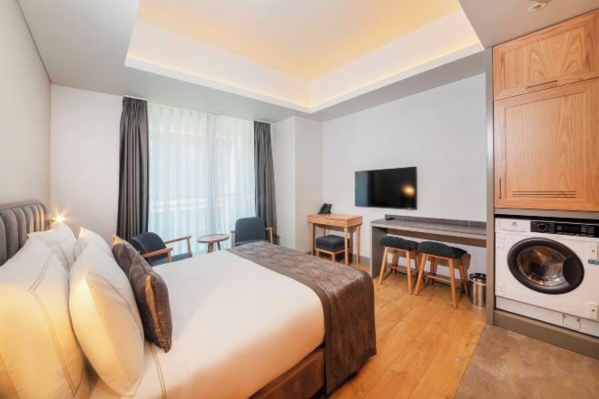 Una habitación de hotel con cama, escritorio, silla, televisor y lavadora.