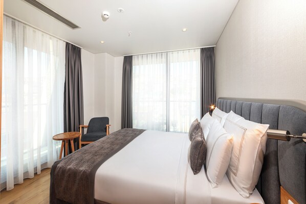 Habitación de hotel con una cama grande, una mesita redonda pequeña, una silla y vistas a través de cortinas translúcidas.