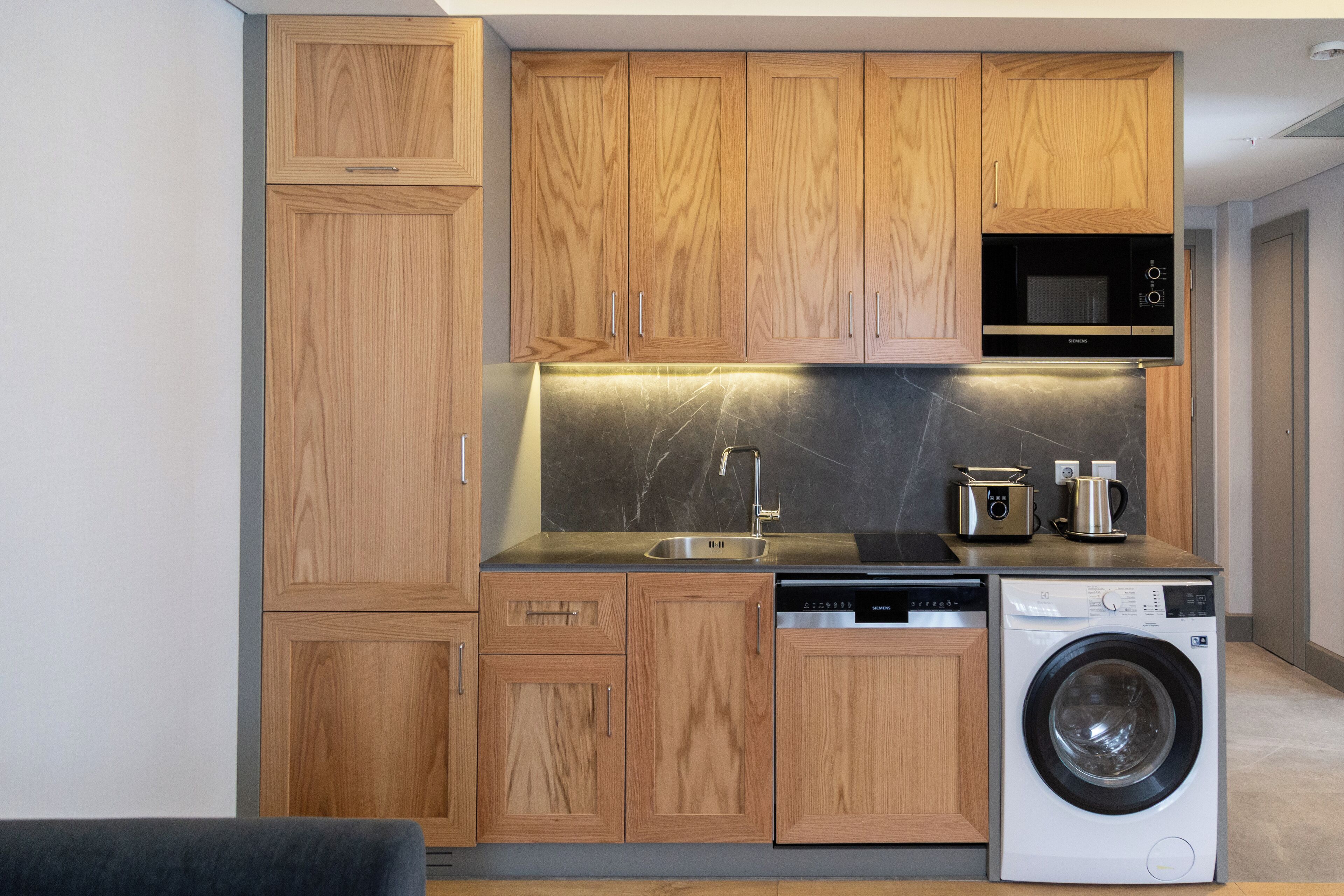 A compact kitchen with wooden cabinets, a microwave, a sink, a dishwasher, and a washing machine.