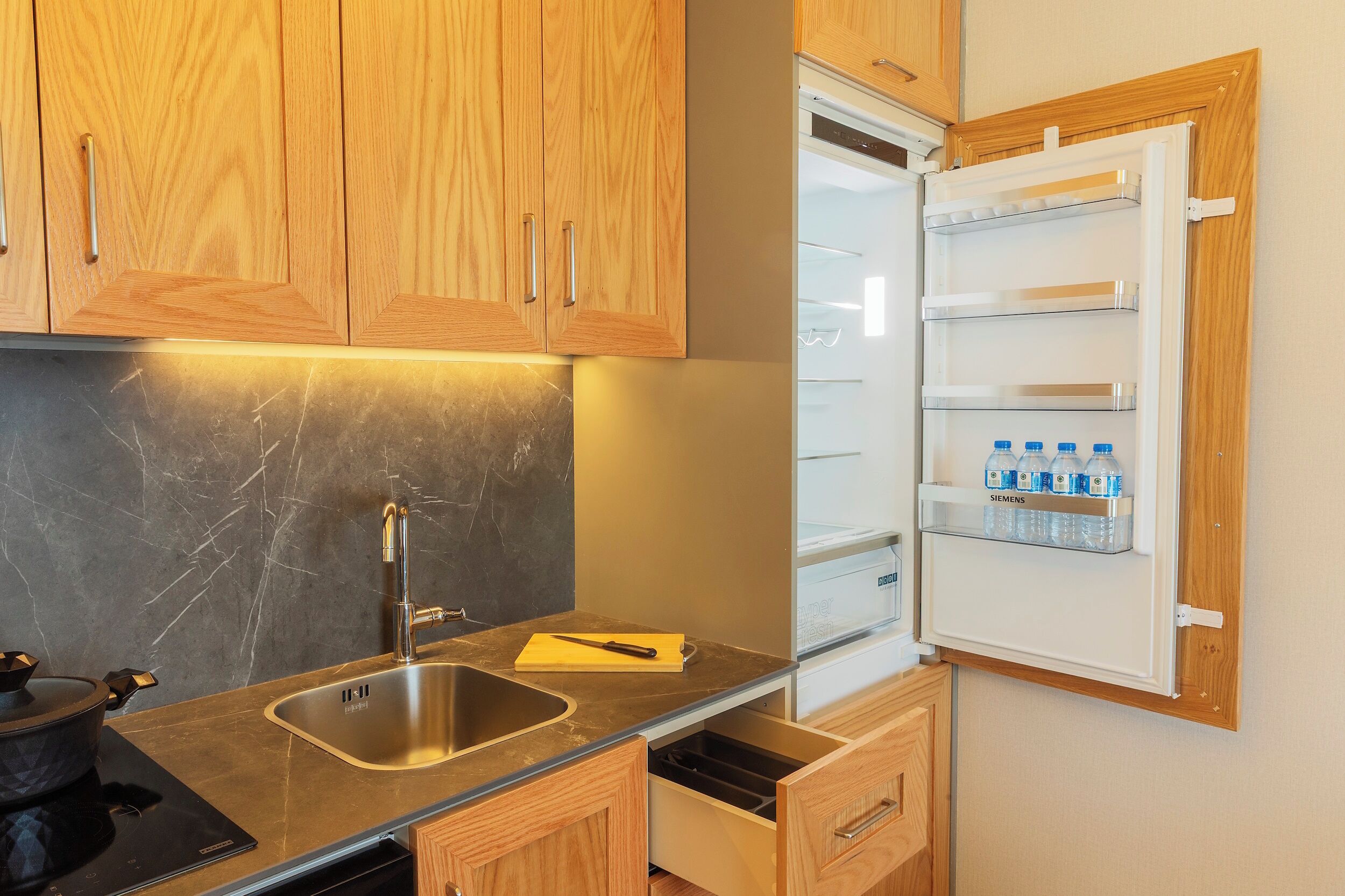 A kitchen with wooden cabinets, a stainless steel sink, and a built-in refrigerator with water bottles.