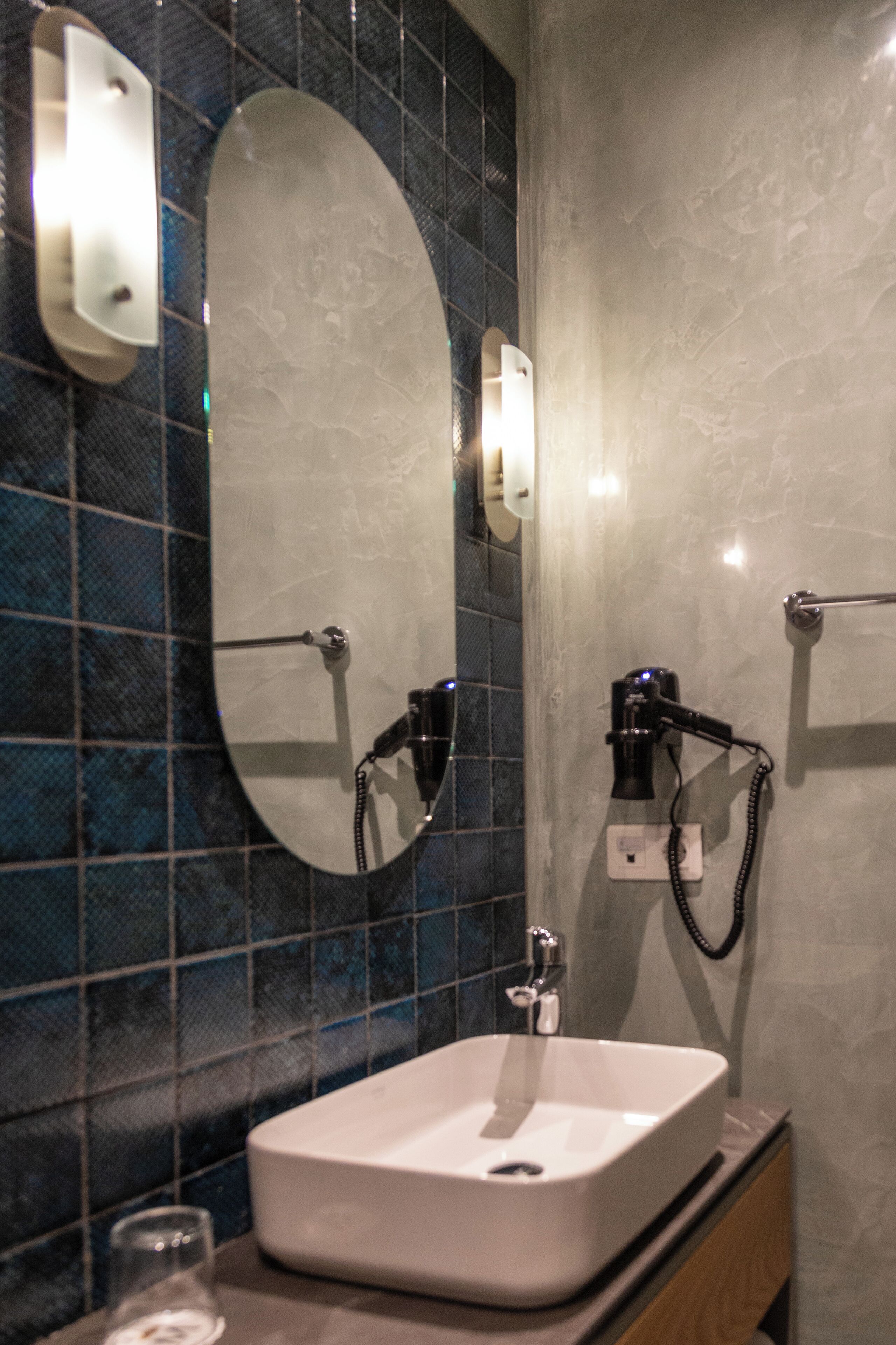 A bathroom with a rectangular sink, a mirror, and a hairdryer mounted on the wall.