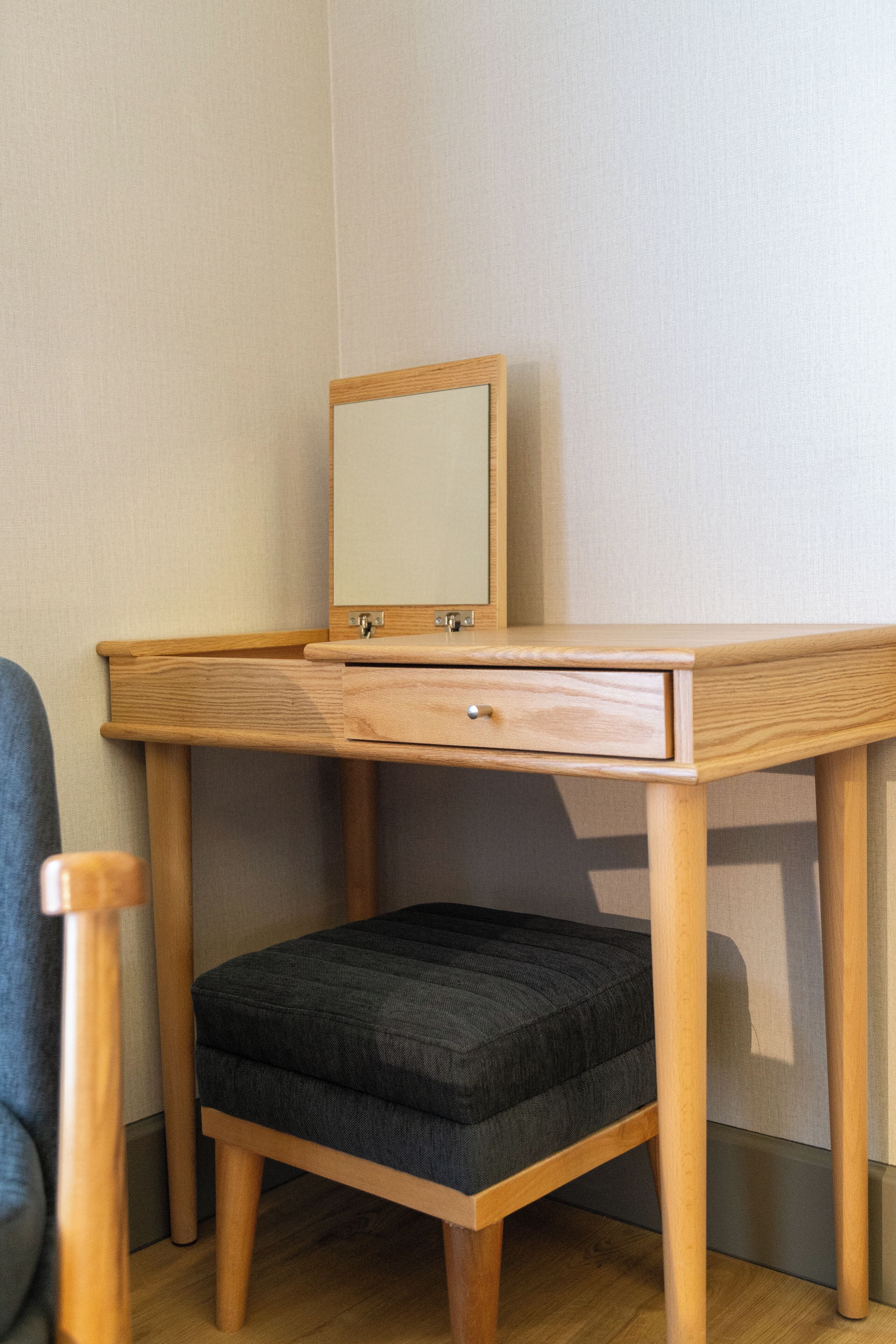 A wooden desk with a mirror, a drawer, and a cushioned stool.