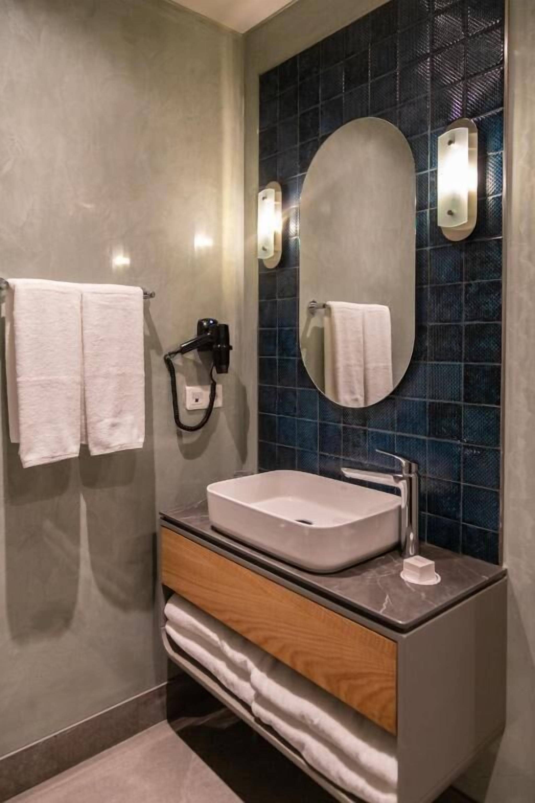 Un baño moderno con un espejo ovalado grande, un lavabo blanco y un perchero con dos toallas.