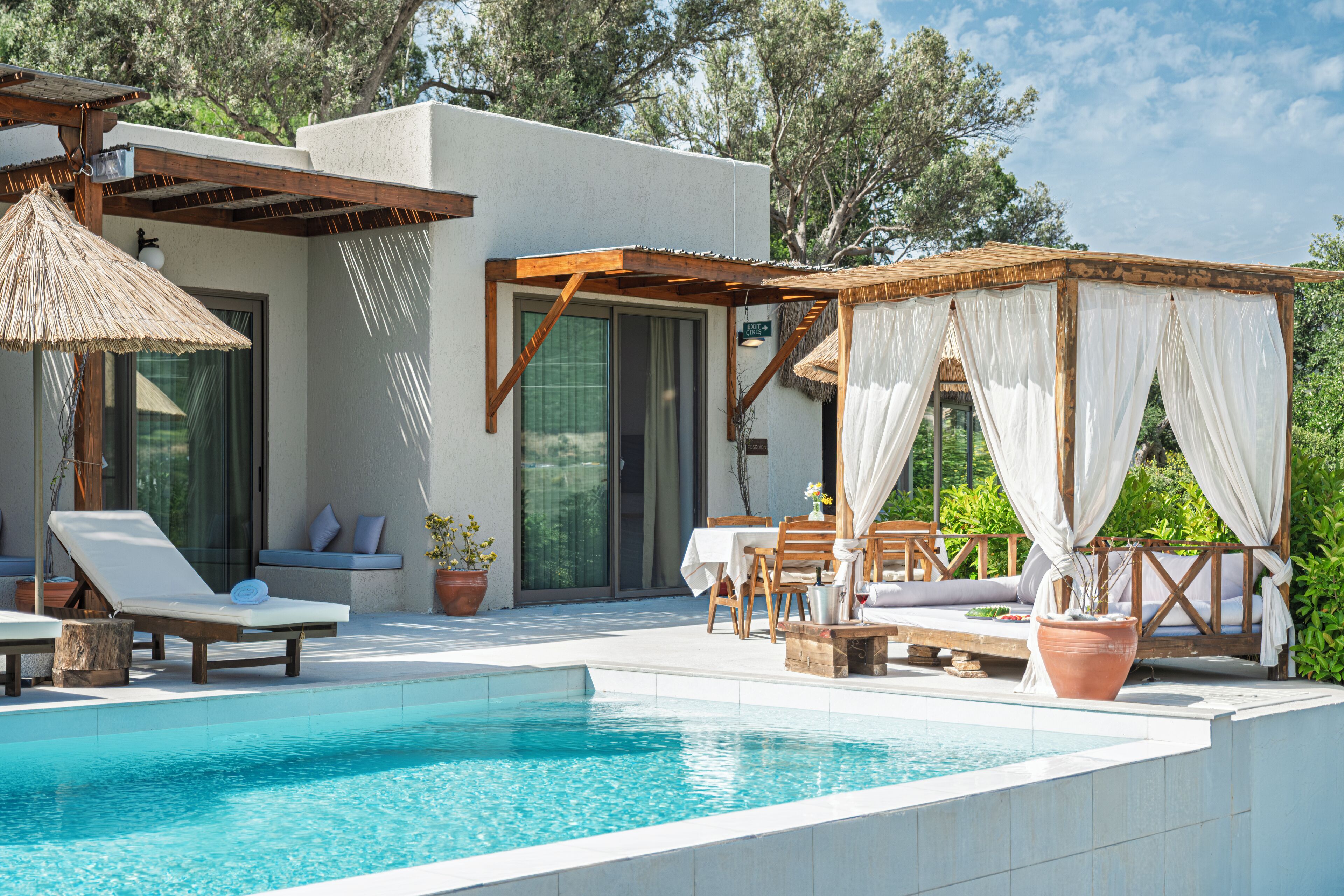 A pool area with lounge chairs, a table, and a covered seating area with curtains.
