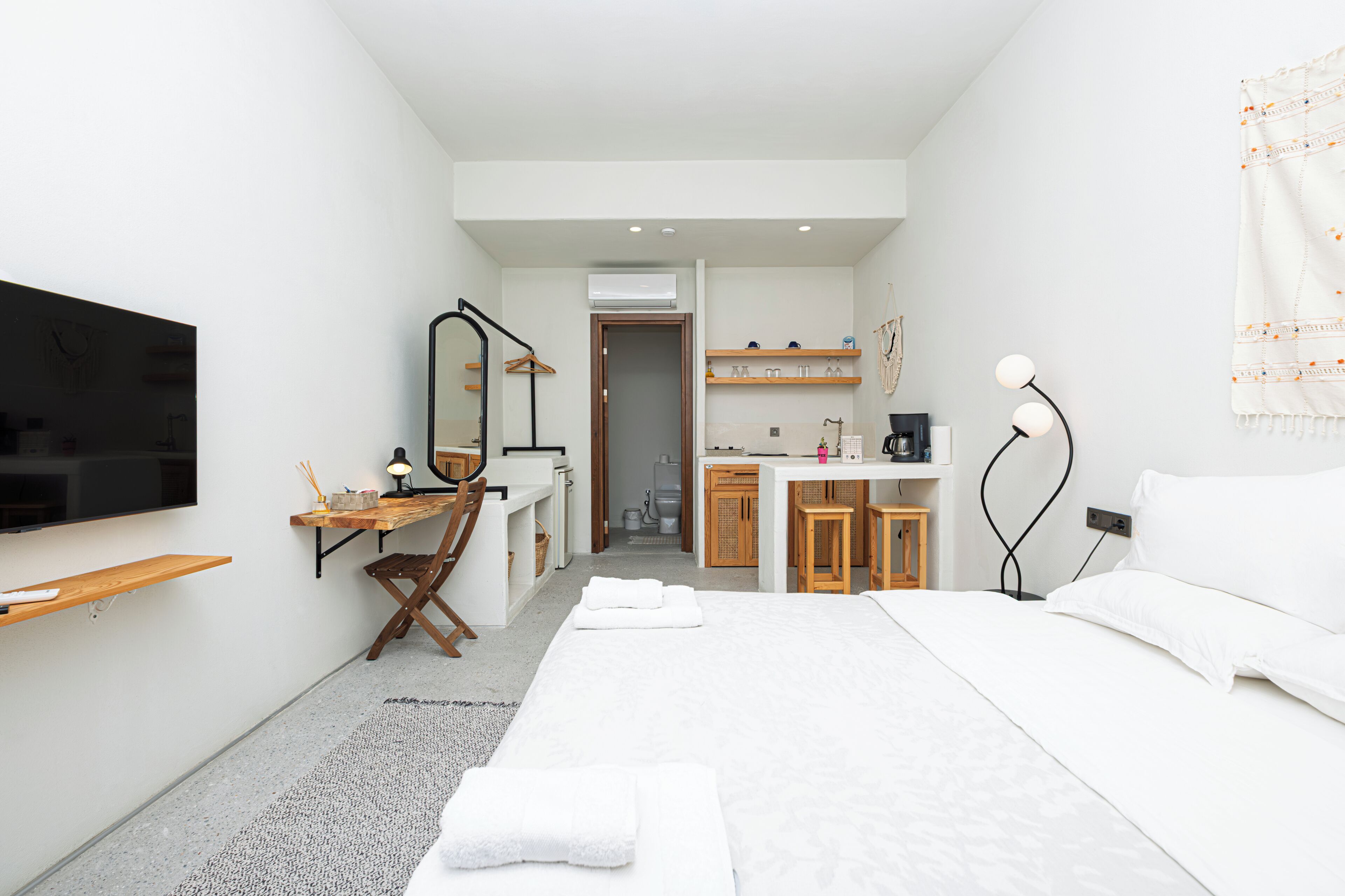 A modern hotel room with a bed, a desk, a TV, and a bathroom visible through an open door.