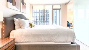 A modern bedroom with a large bed, a nightstand, and a view of the city through large windows. - Luxury & Bright Apt Downtown Seaport (Boston MA)