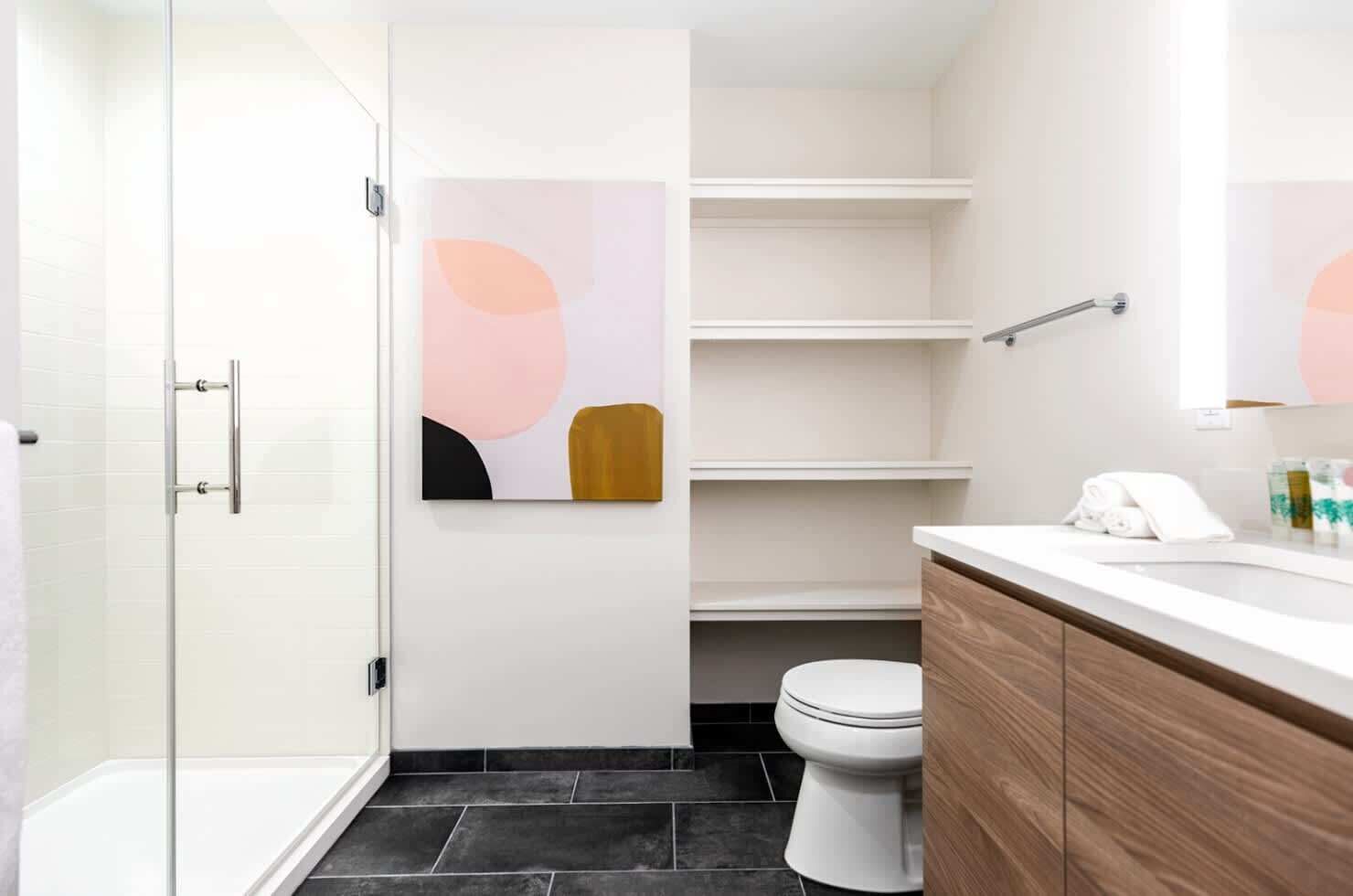 Un bany modern amb una cabina de dutxa de vidre, un vàter blanc i un moble de tocador de fusta amb un mirall.
