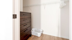 A room with a wooden dresser, a white laundry basket, and a metal shelf with hanging clothes. - Luxury & Bright Apt Downtown Seaport (Boston MA)