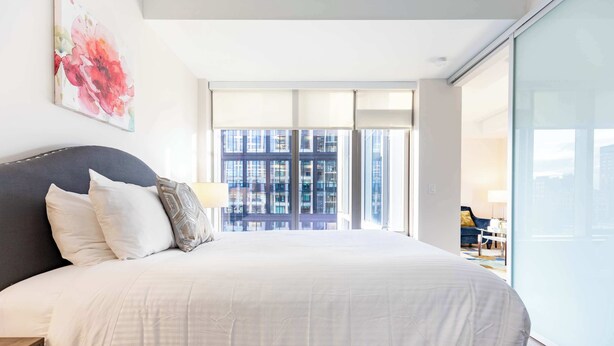A modern hotel room with a large bed, a view of the city through floor-to-ceiling windows, and a minimalist decor.