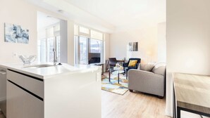 A modern apartment with a kitchen, dining area, and living room. It features large windows, a sofa, and a coffee table.
