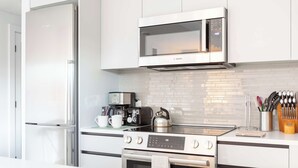 A modern kitchen with white cabinets, a Bosch microwave, a coffee maker, a kettle, and an oven.
