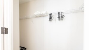 A laundry area with a metal rack, a black laundry basket, and a white wall.