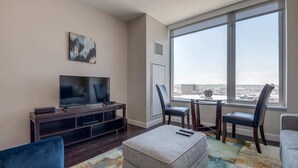 A modern living room with a flat-screen TV, a coffee table, and a dining area with chairs and a small table.