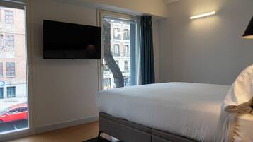 Un dormitorio con una cama, un televisor montado en la pared y una ventana con cortinas.