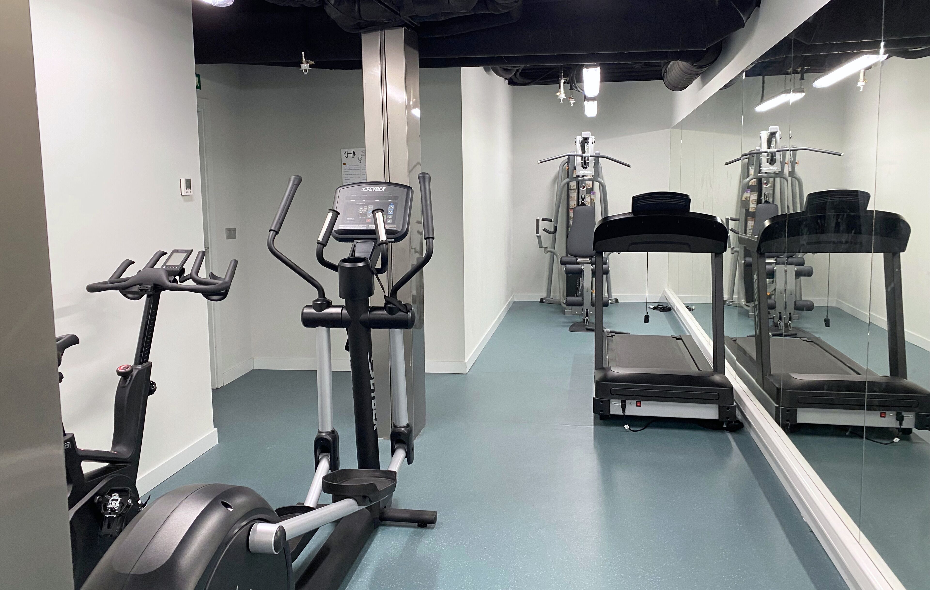 Een fitnessruimte met cardioapparaten, krachttrainingsmachines en een spiegelwand.