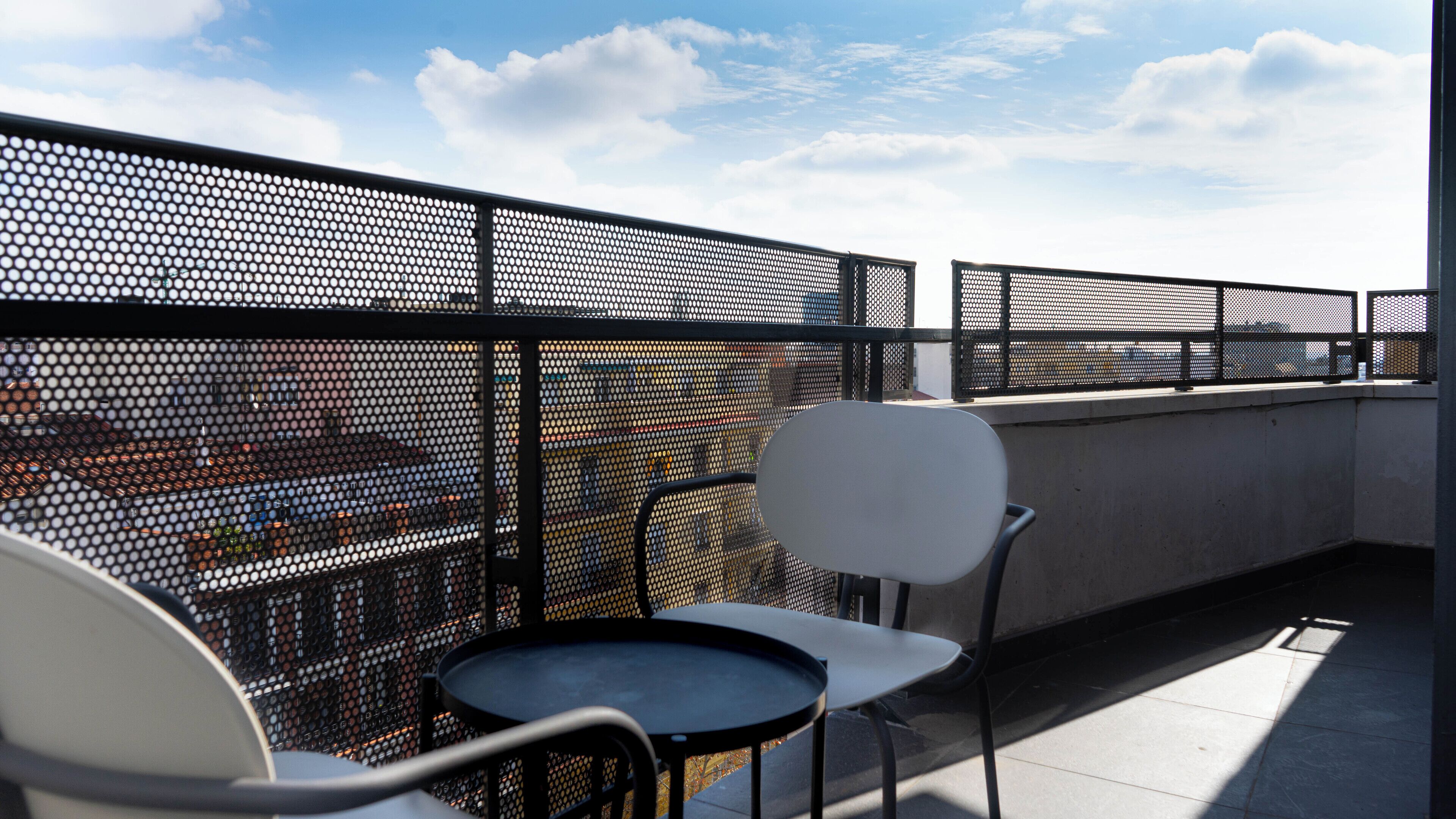Una terraza en la azotea con cerramiento metálico, dos sillas y una mesa redonda pequeña.