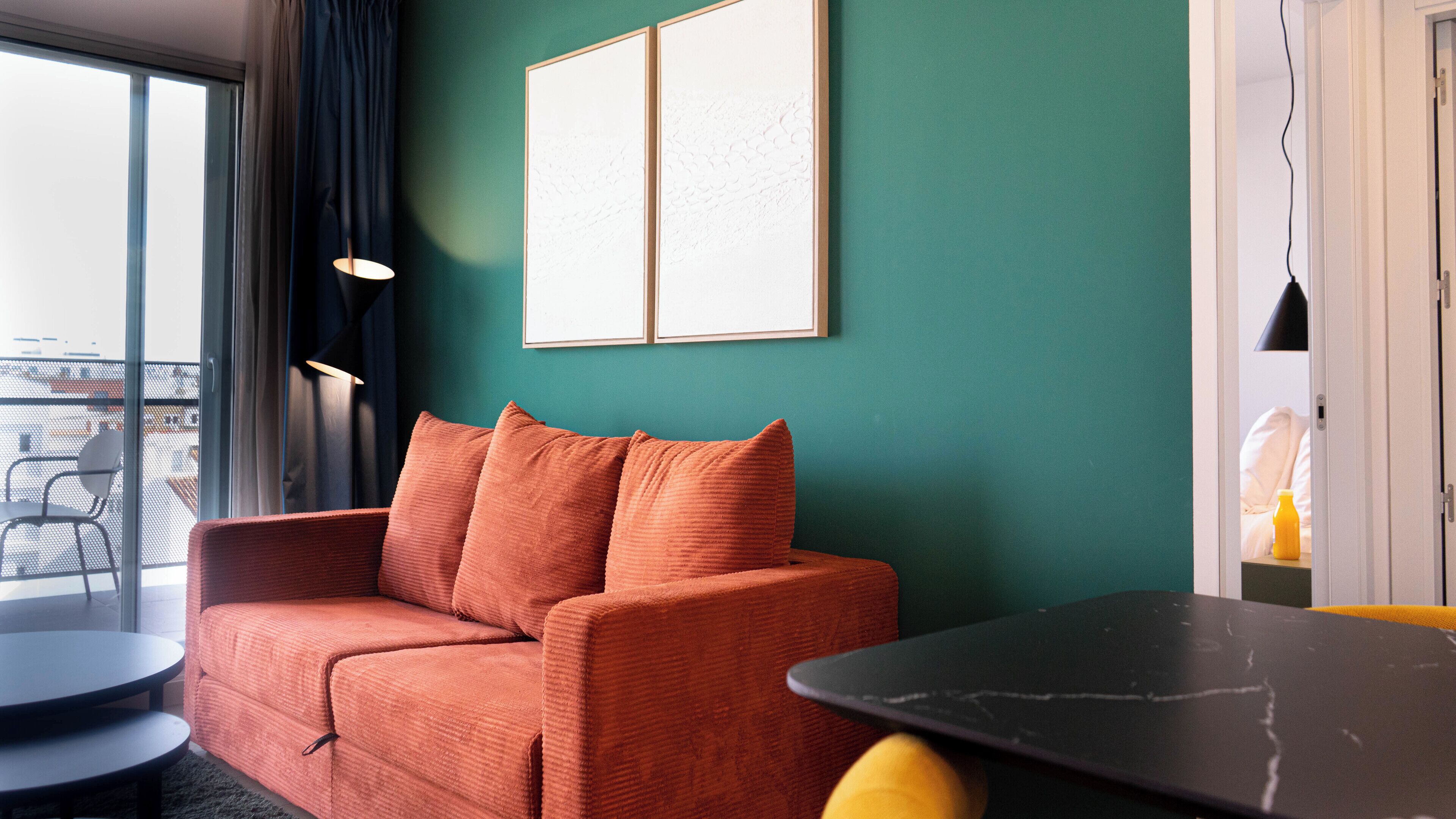 Une pièce avec un mur de couleur turquoise, un canapé rouge, une table noire et une petite table ronde.