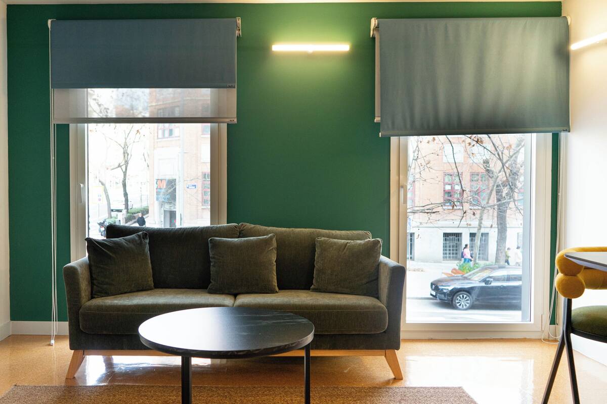 A living room with a sofa, a coffee table, and two windows with blinds.
