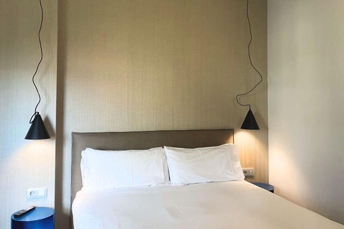 A neatly made bed with white linens and a wooden headboard, flanked by two black lamps on either side.