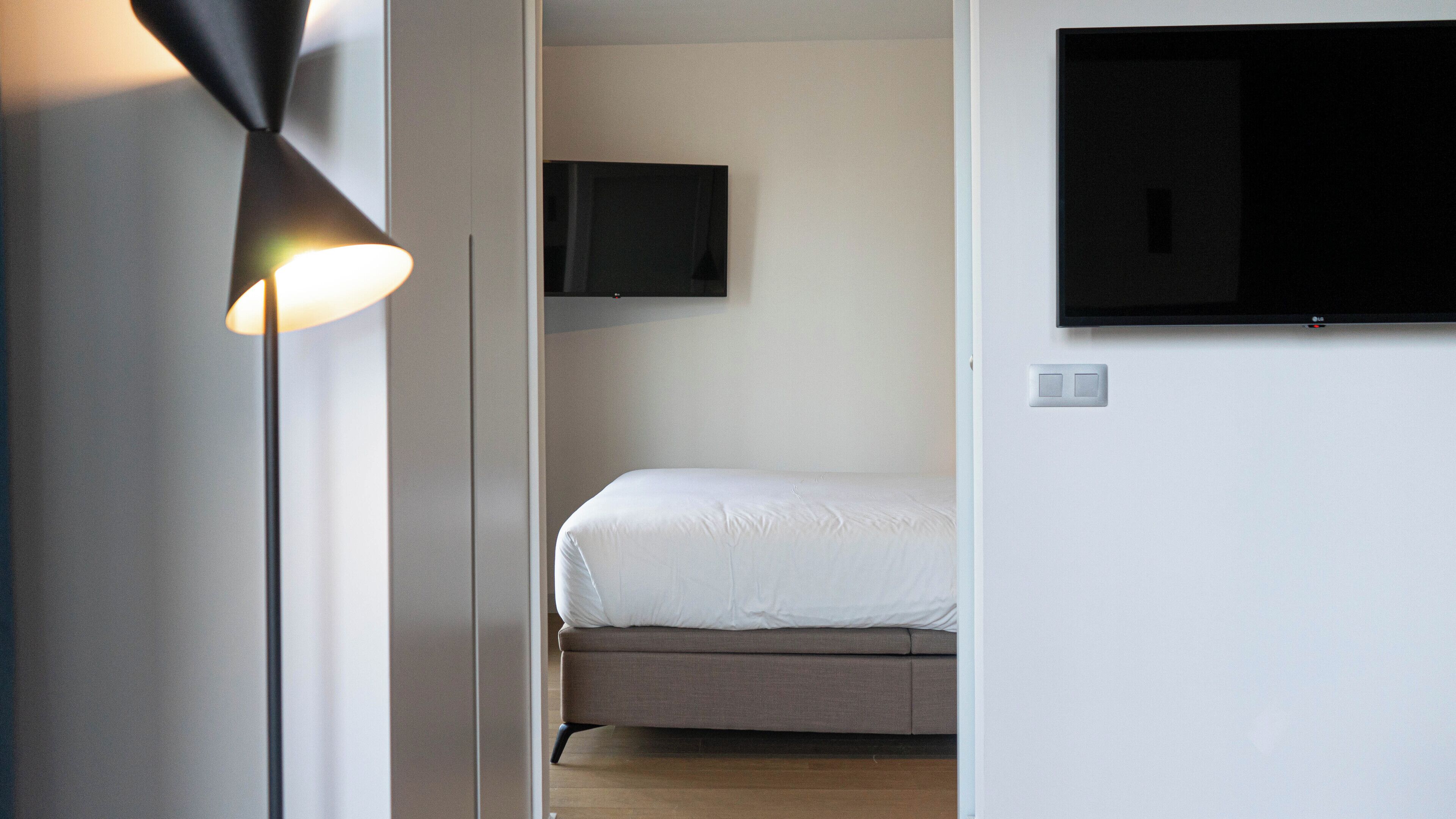 Une chambre à coucher avec un lit, un téléviseur fixé au mur et une lampe sur pied.
