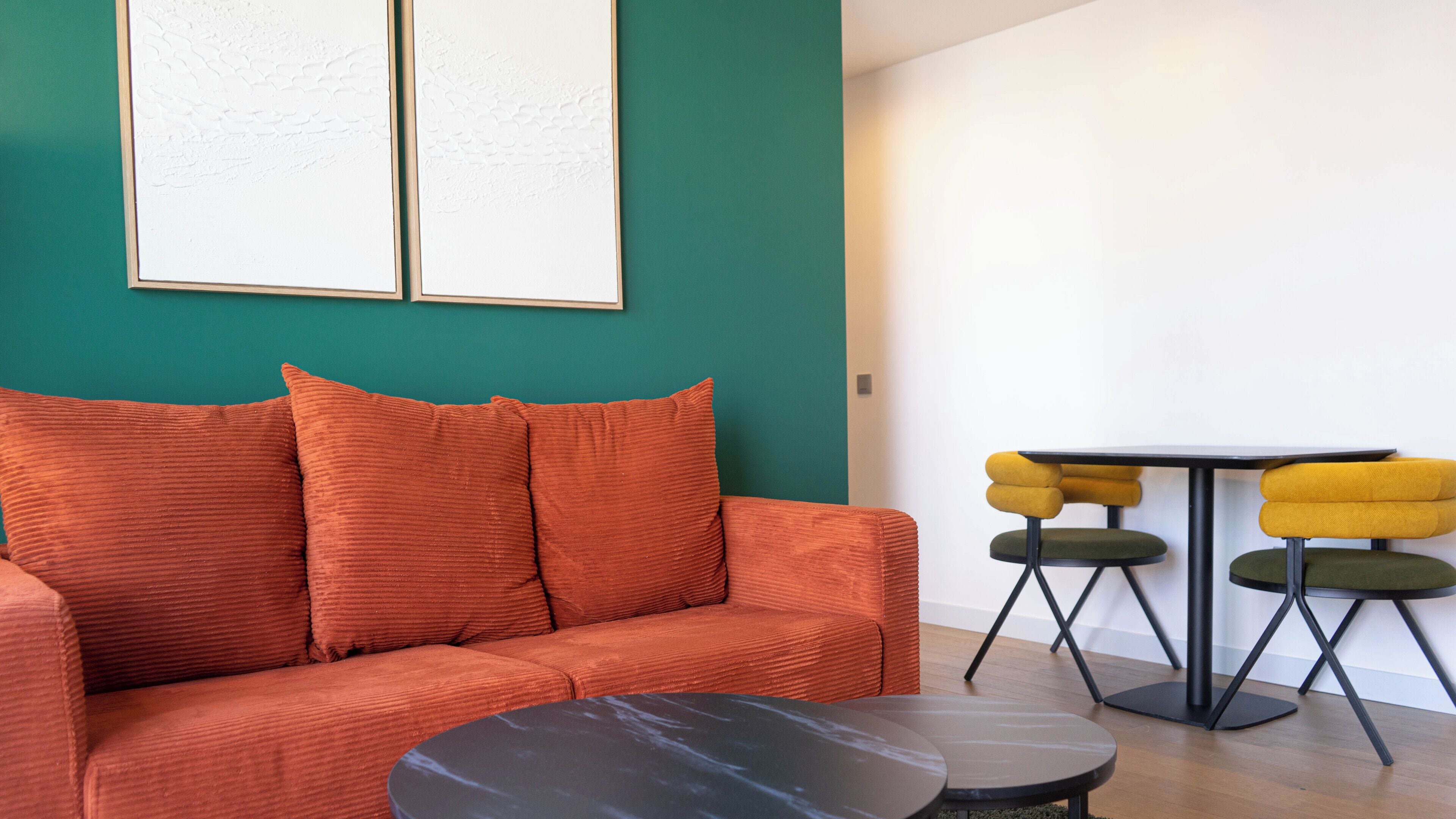 A modern living room with a teal accent wall, a red sofa with cushions, a black coffee table, and a small round table with yellow chairs.