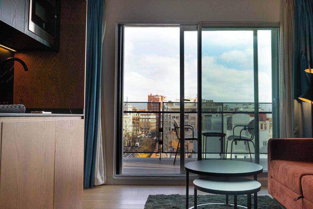 A modern living room with a sofa, a small table, and a view of the city through large glass doors.