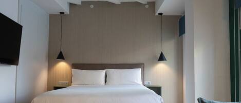 A modern hotel room with a large bed, two bedside tables, a flat-screen TV, and pendant lights.