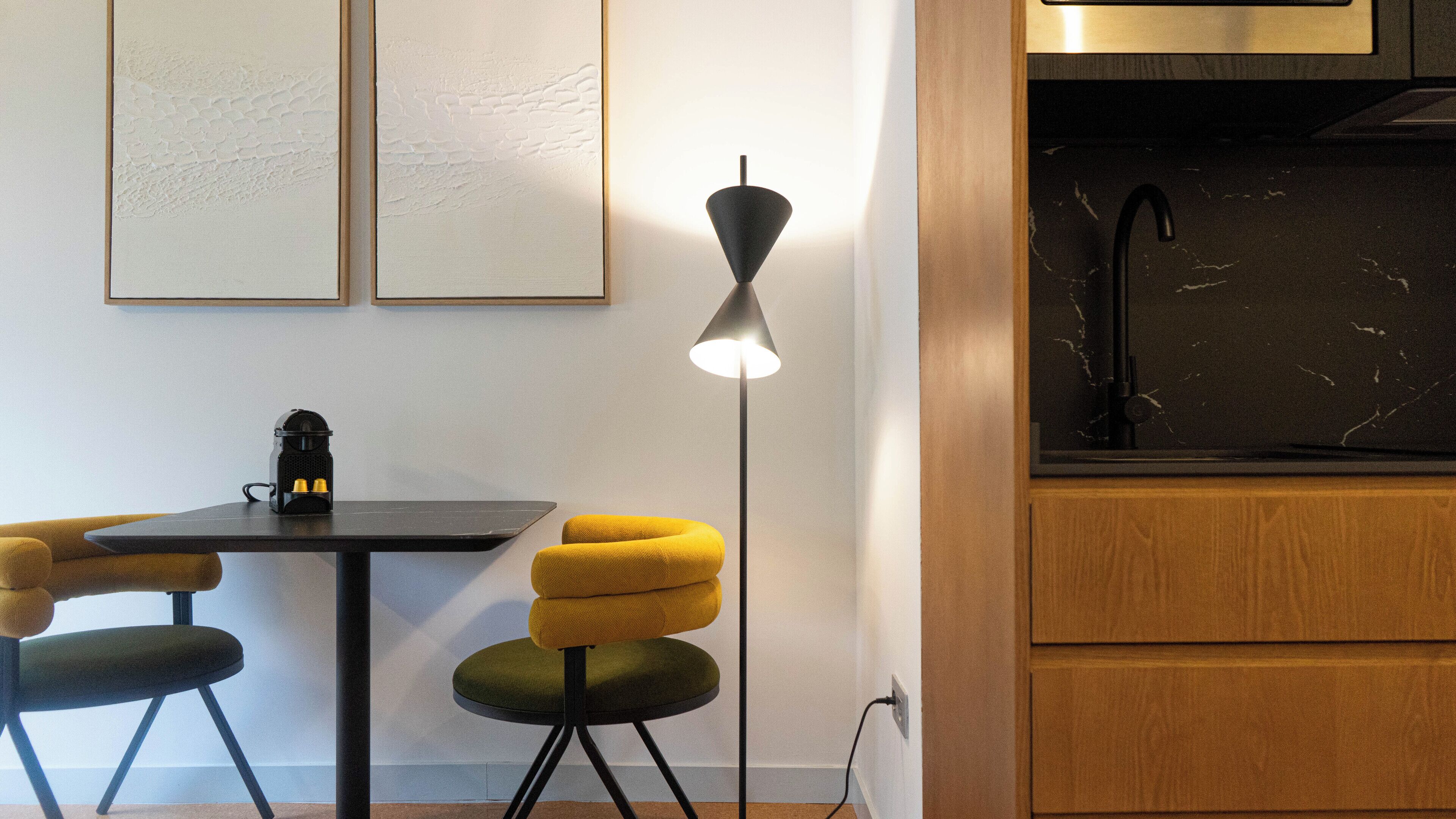 Une cuisine moderne avec un plan de travail noir, une machine à café et une chaise jaune.