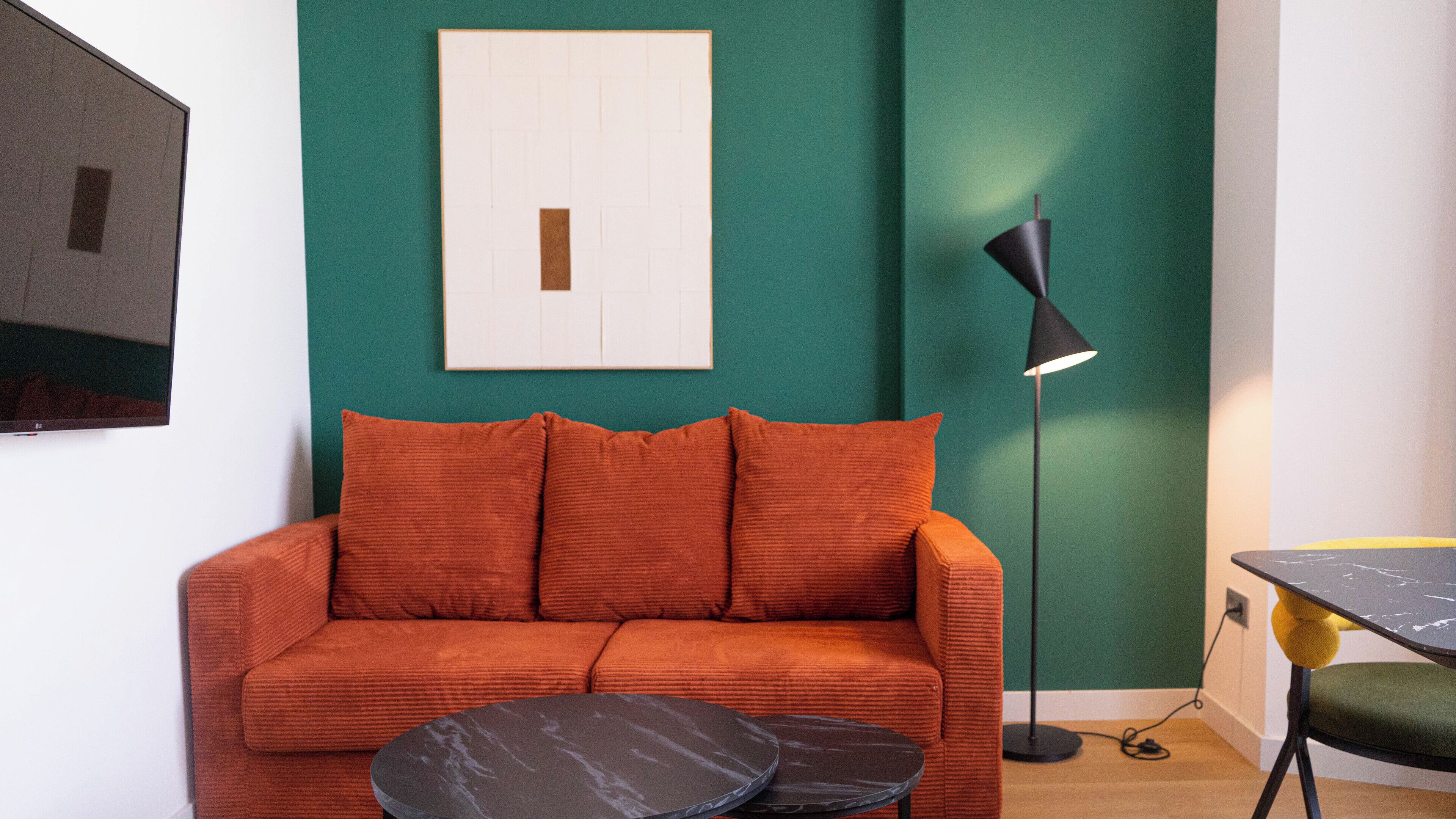 A living room with a teal accent wall, a red sofa, two black round side tables, a floor lamp, and a framed picture.