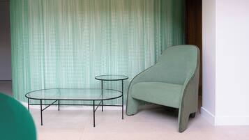 Una habitación con pared de diseño verde, un sillón verde y una mesita de cristal con patas metálicas.