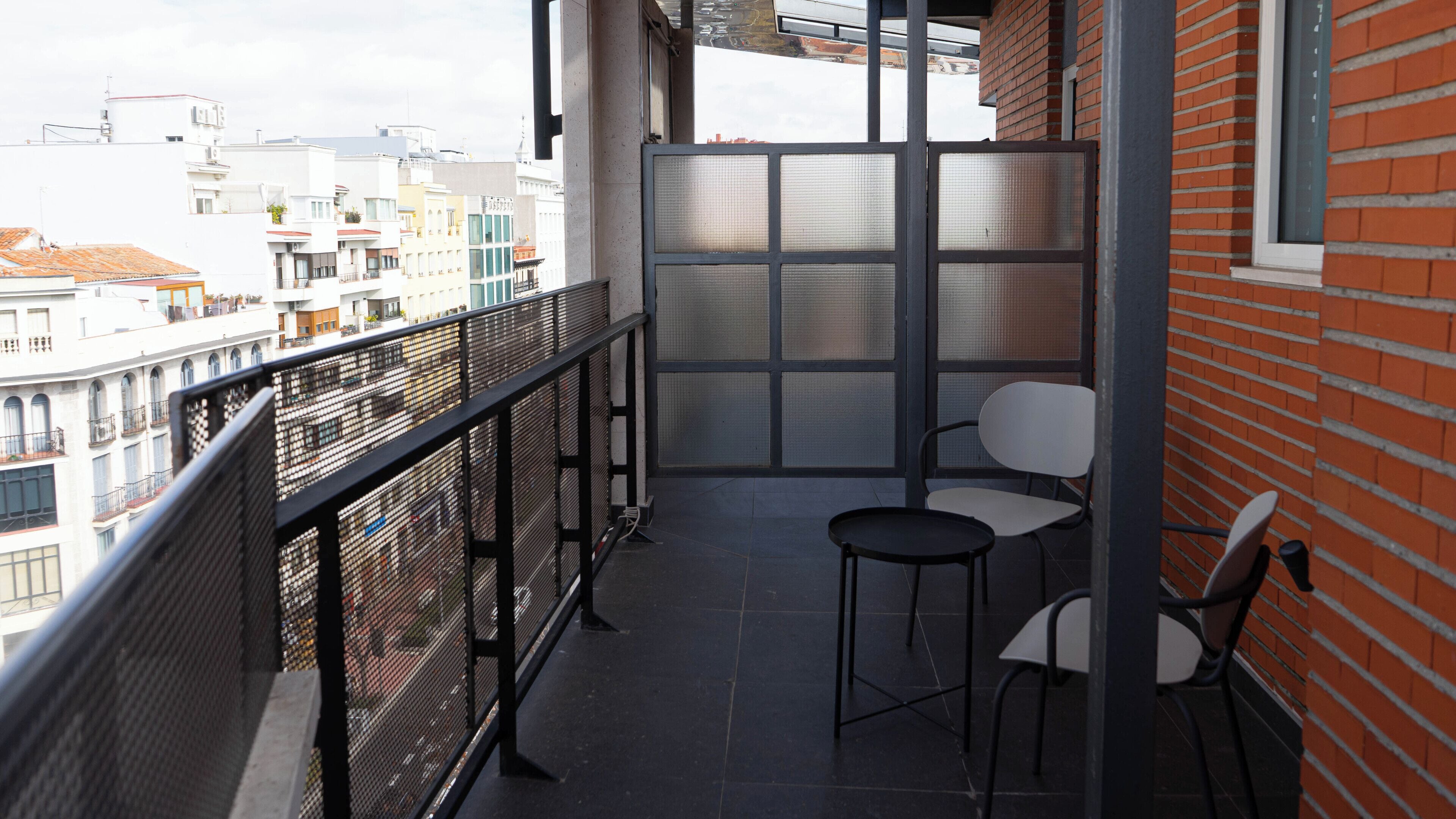 A balcony with two chairs, a metal railing, and a view of city buildings.