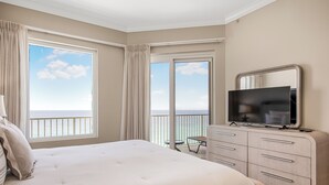 Habitación de hotel con cama, televisor, cómoda y balcón con vista al océano.