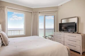 A hotel room with a bed, a TV, a dresser, and a balcony with a view of the ocean.