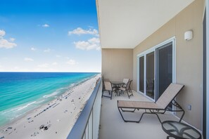 Un balcon avec vue sur la plage et l’océan, une table avec des chaises et un fauteuil de relaxation.