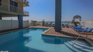Una piscina con sillas de descanso, vista al mar y un edificio con balcones.
