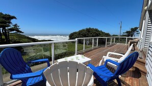 A wooden deck with two blue Adirondack chairs and a small table, overlooking a coastal view. - Soaring Seabird - Yachats Ocean View with Hot Tub (Yachats)
