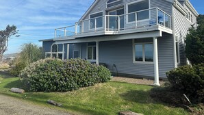 A two-story house with a balcony, large windows, and a well-maintained lawn. - Soaring Seabird - Yachats Ocean View with Hot Tub (Yachats)