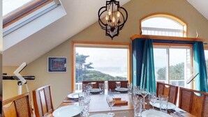 A dining area with a table set for four, a chandelier, and a view of the outdoors. - Soaring Seabird - Yachats Ocean View with Hot Tub (Yachats)
