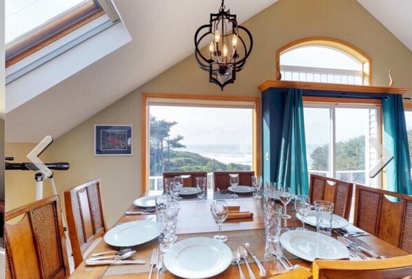 A dining area with a table set for four, a chandelier, and a view of the outdoors. - Soaring Seabird - Yachats Ocean View with Hot Tub (Yachats)