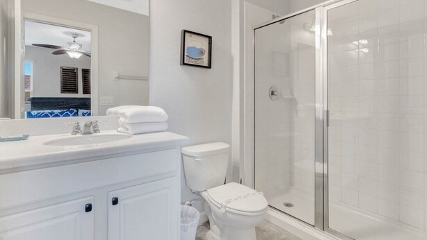 A modern bathroom with a white vanity, a toilet, and a glass-enclosed shower. - Upstair Loft Premium Home With Pool, Spa & Games! 5 Bedroom Condo (Davenport)