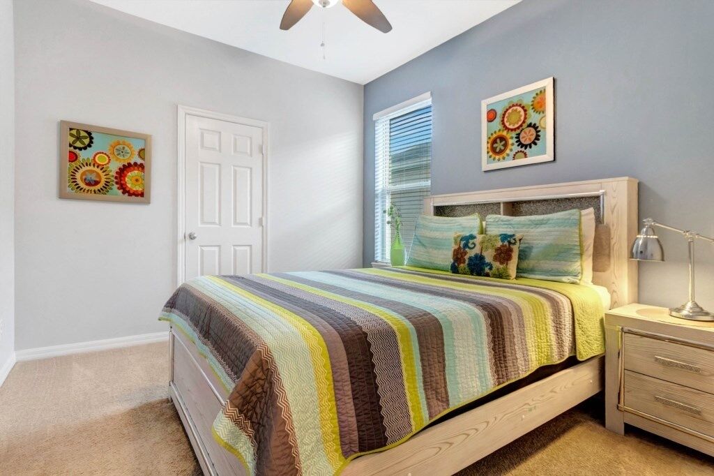 A bedroom with a bed, a nightstand, a ceiling fan, and two wall-mounted paintings.