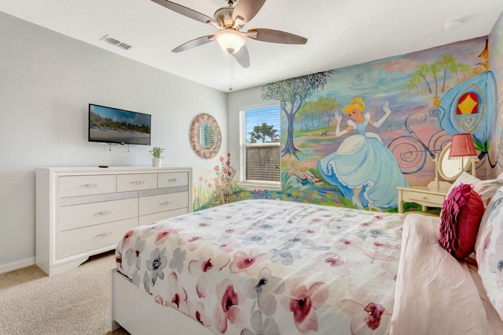 A bedroom with a bed, a ceiling fan, a TV, a dresser, a window, and a mural on the wall.