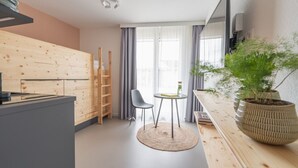 Quarto moderno e compacto com cozinha americana, área de refeições e um espelho grande.