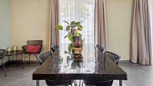 Un comedor con una gran mesa rectangular, sillas negras, una planta en maceta y un cojín rojo en una silla.