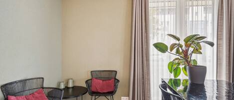A small, well-lit room with two chairs, a table, a potted plant, and a window with curtains.